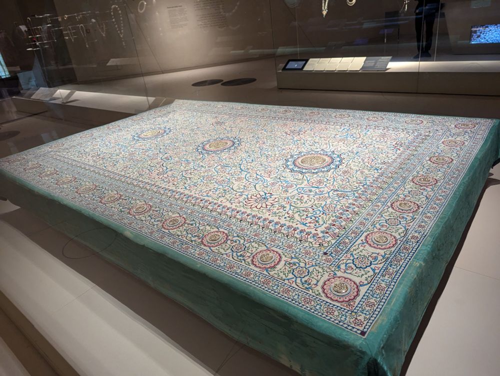 An intricately beaded carpet about 6 x 5 feet in museum display 