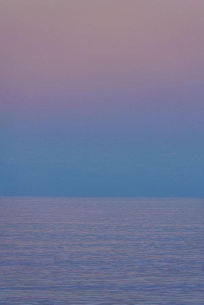 Hulhumalé, Maldives. Sunrise Blue Hour at sea. Photo was taken between blue and golden hour. Foreground is a very calm blue sea with light pink shade. From horizon to mid sky is blue. Above that is light pinkish purple. 