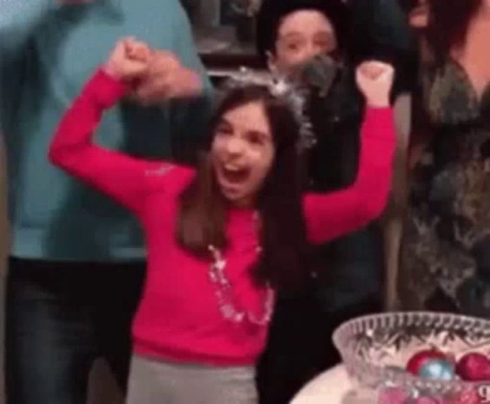 a girl in a pink sweater is raising her arms in the air while standing in front of a group of people .