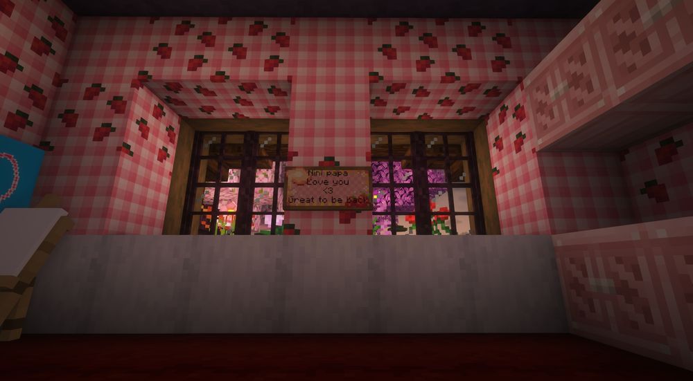 A minecraft screenshot of an almost empty bedroom with pink checkered wallpaper adorned with strawberries. 

There's one of Aspen's signs saying "nini papa I love you <3 happy to be back" from their first night in the season 2 world.