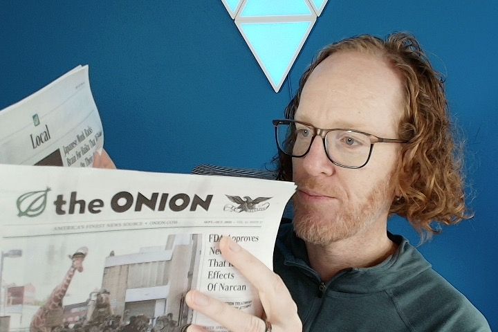 Robby Russell reading a paper copy of The Onion