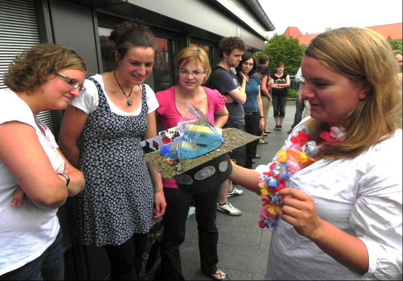 A group of people standing around a person holding a intensely decorated PhD/graduation hat.