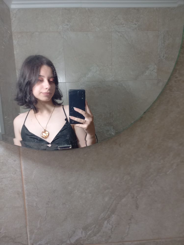 Uma foto minha em um espelho. Estou com o cabelo curto, preto, e ligeiramente ondulado.