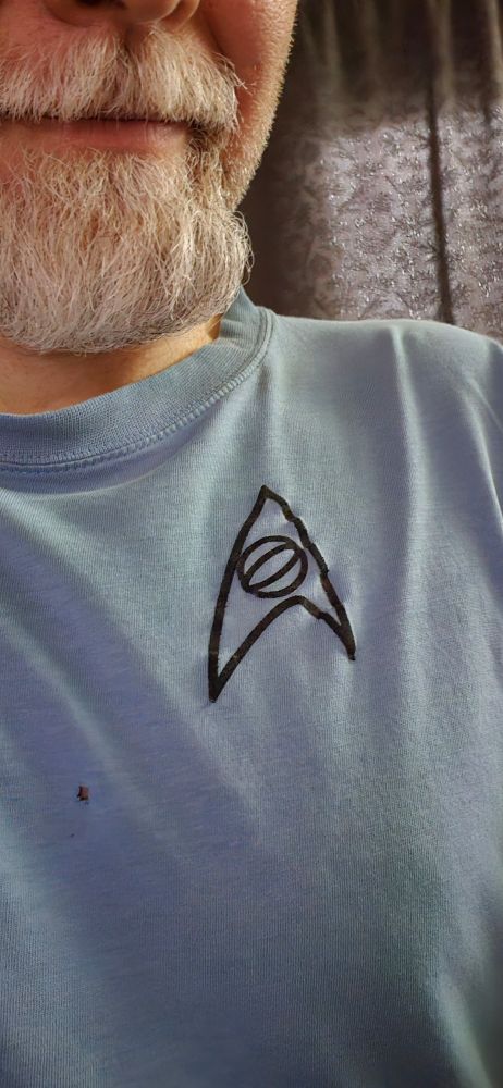A handsome goateed man is wearing a blue shirt with an insignia from the original Star Trek tv series.