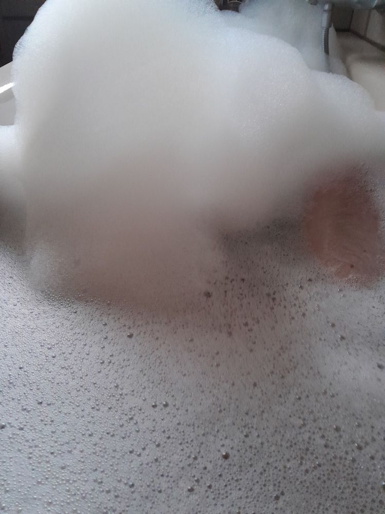 Badewanne mit Wasser, Schaum und Teilen der Armatur und des Beins aus der Sicht des Badenden 