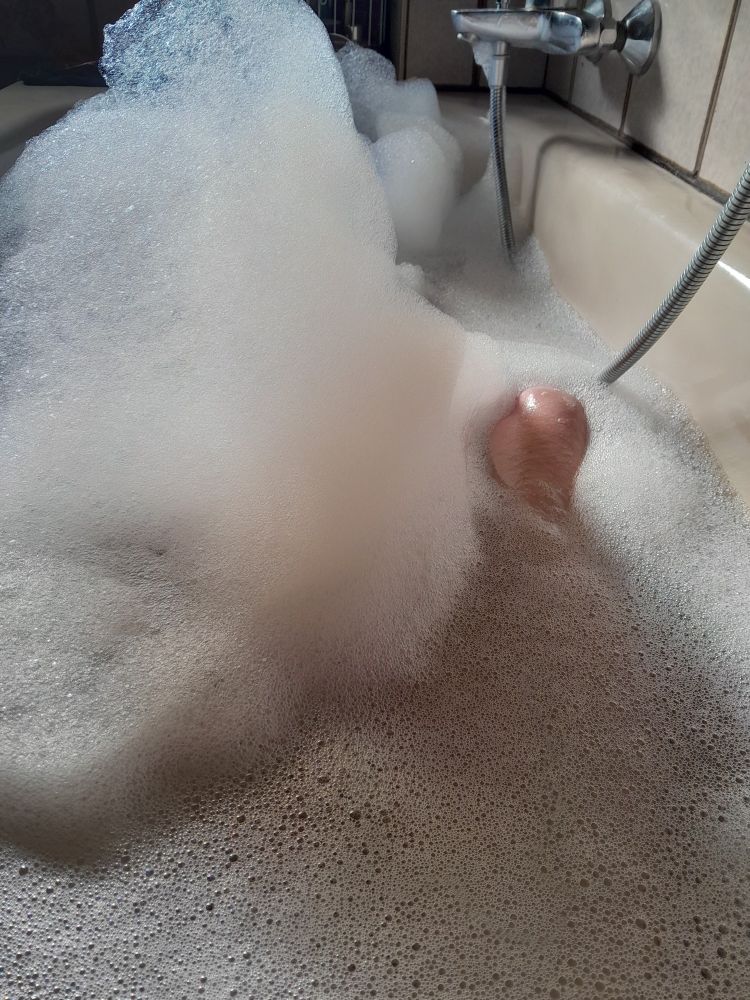 Badewanne mit Wasser und Schaum sowie Teilen der Armatur und des Körpers aus der Sicht des Badenden