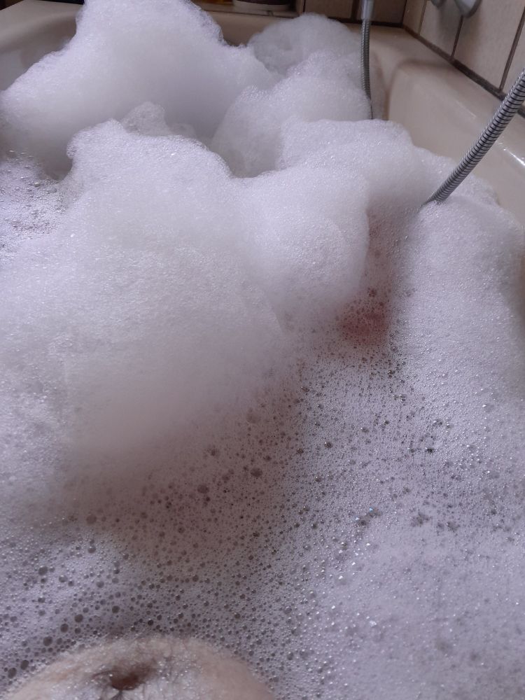 Badewanne mit Wasser und Schaum sowie Teilen der Armatur und des Körpers aus der Sicht des Badenden 