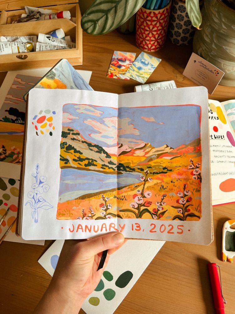 a gouache painting in my sketchbook. you can see a lake, mountains and flowers in the foreground. warm tones. 