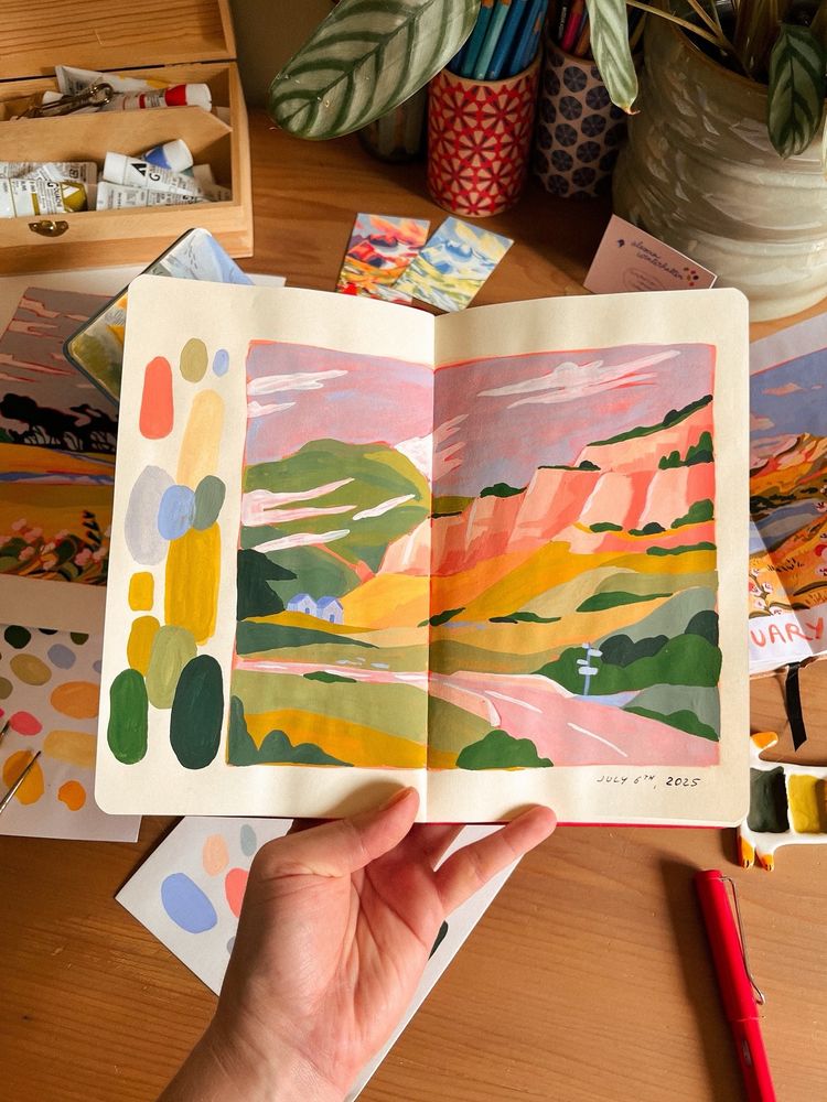 a gouache painting in my sketchbook. there’s a road, a pink cliff and two tiny blue houses. 