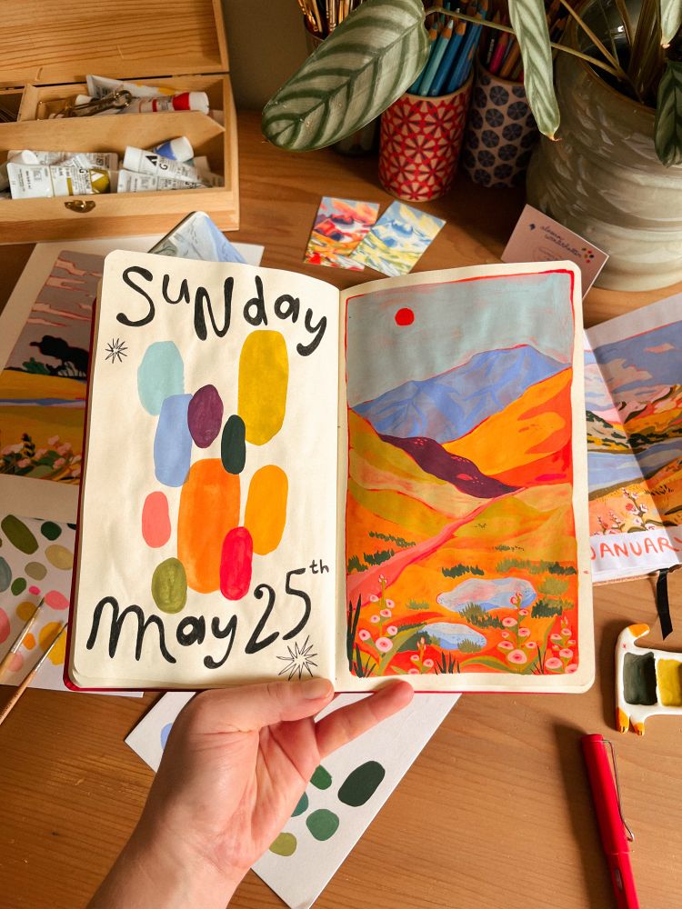 a gouache painting in my sketchbook. there’s a path going between the mountains and some flowers in the foreground. on the left page is written the date and the color palette is laid out. 
