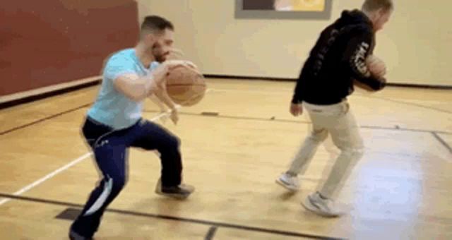 two men are playing basketball on a court and one is dribbling the ball .