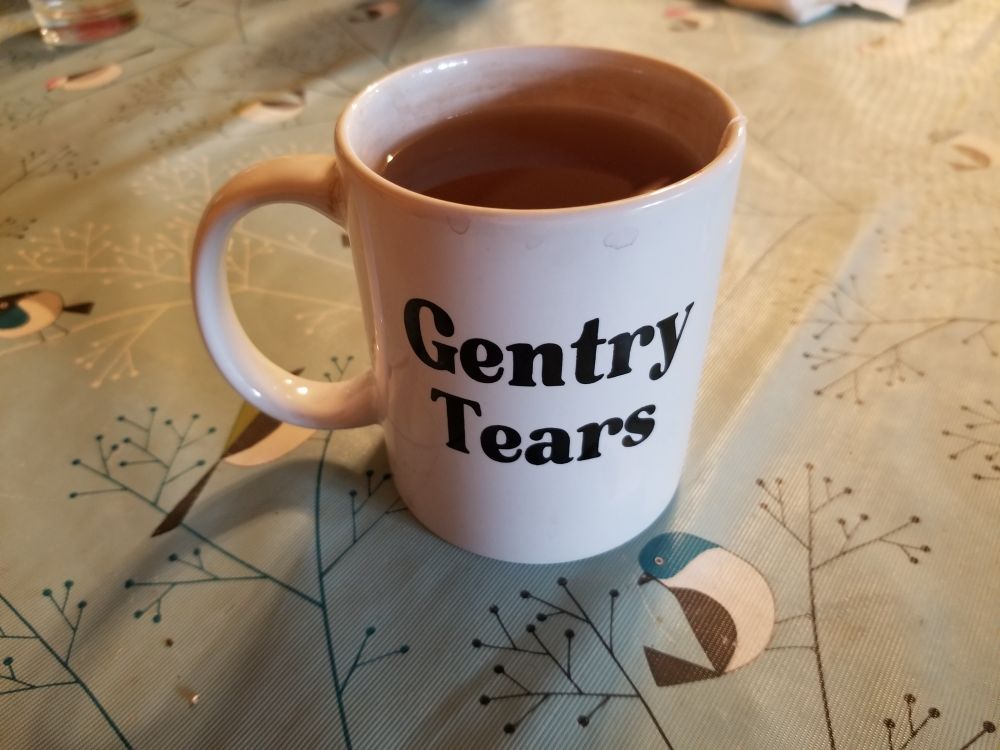 An Asheville Blade mug with tea in it and "gentry tears" in black lettering