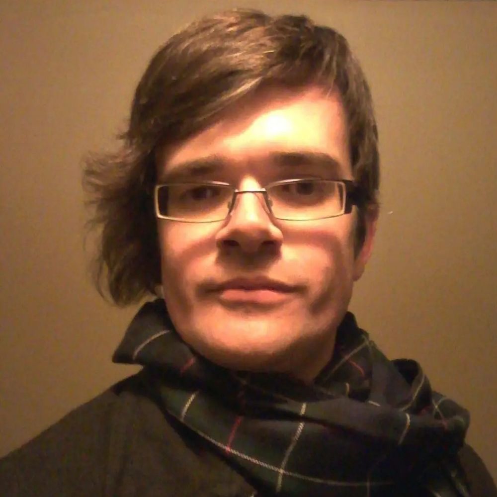 David, a white trans woman, very early in her transition, with slightly long hair, a scarf and a fairly somber expression