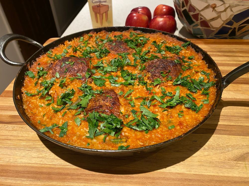 A big fry pan filled with smokey red tinged rice, four seared chicken thighs nestled within 