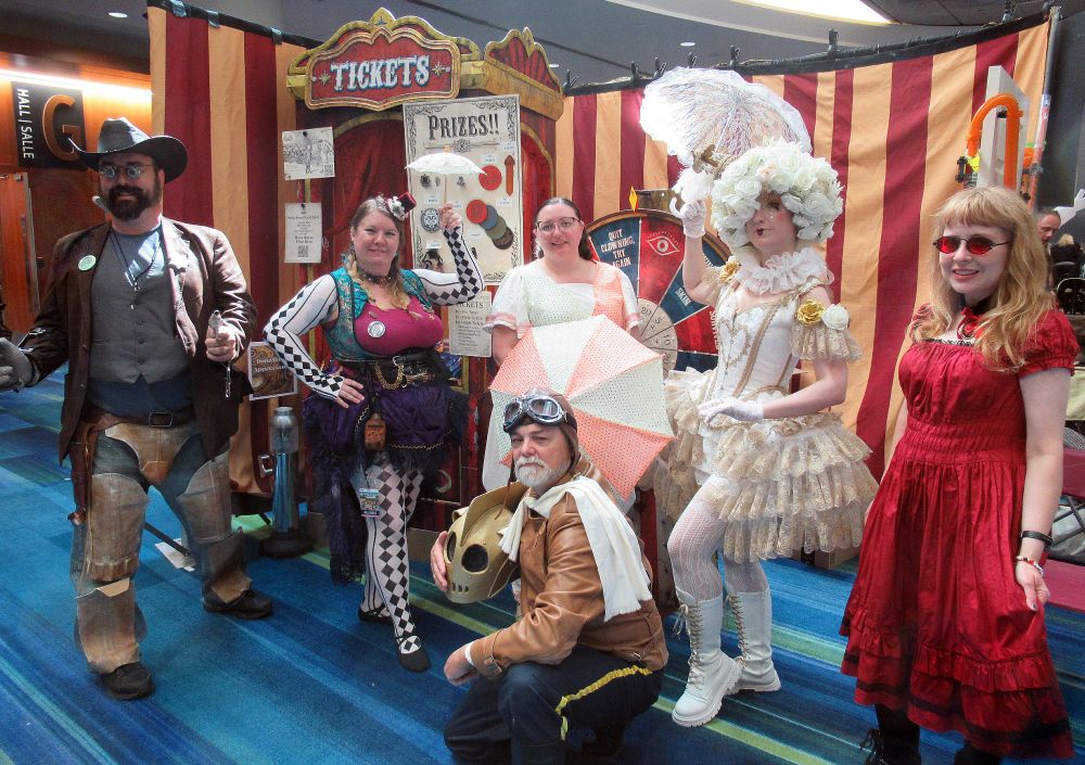 Photo from Fan Expo 2025. A group of people wearing Steampunk costumes standing in front of a carnival display.