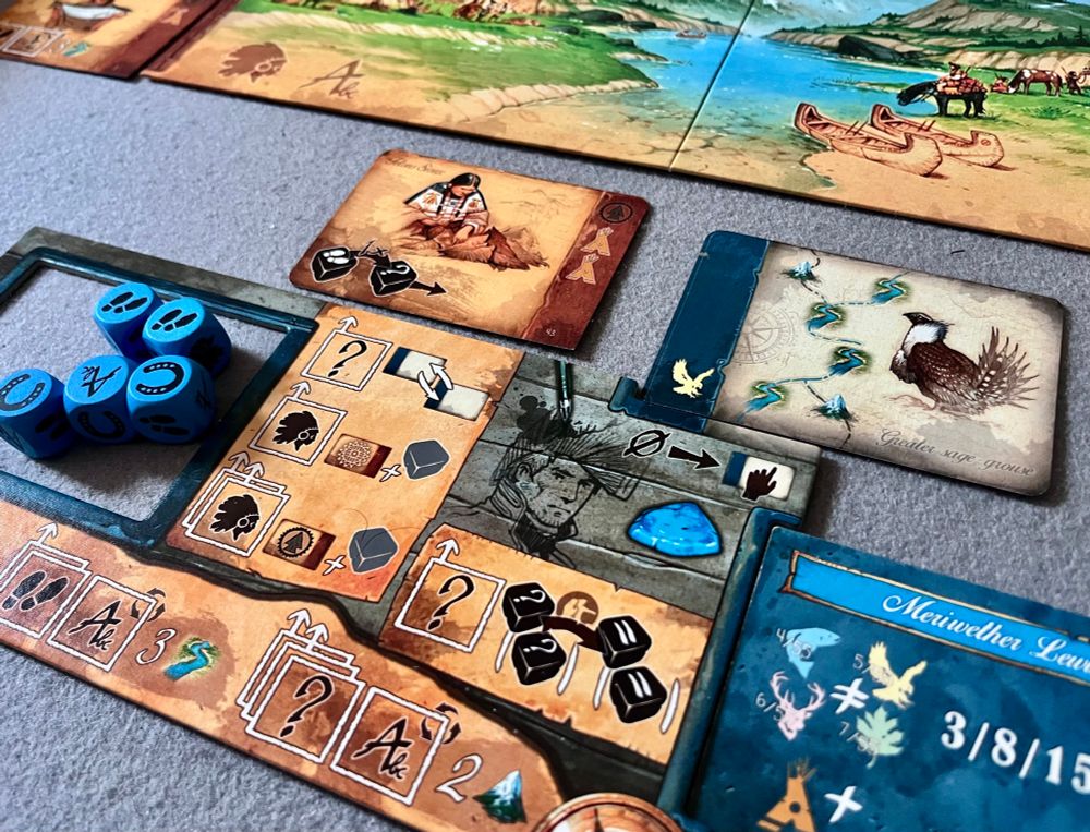 A cardboard player board showing icons for various actions. A cutout holds a pool of 5 blue dice. Cards showing expedition routes and additional actions sit above it. 