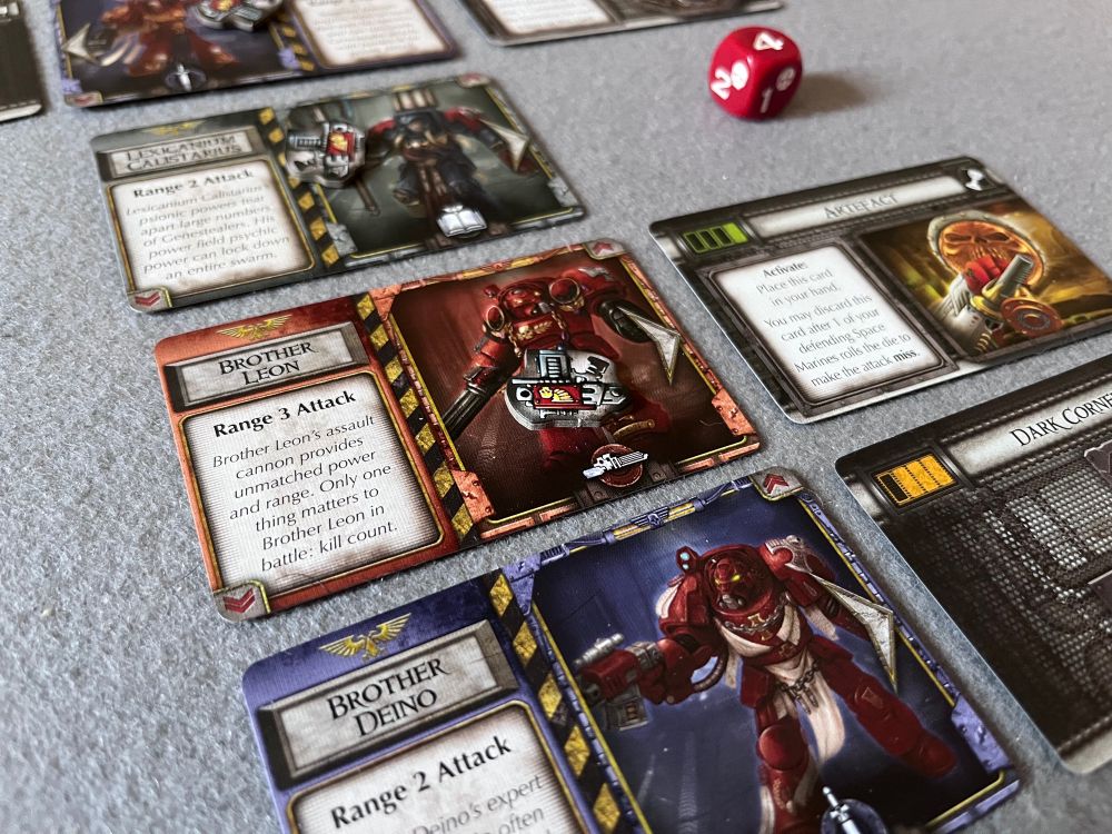Grey, red and purple cards in a vertical line showing space marine illustrations and flavour text. Cards showing terrain types are next to some of the space marines. A red die in the background shows the number 4