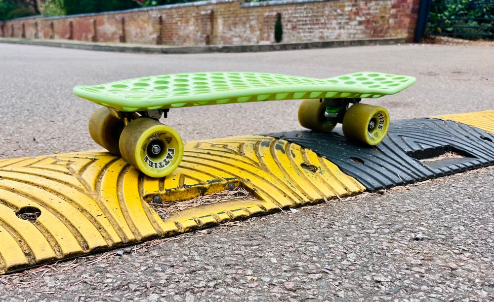 A side view of a green plastic skateboard sat in a yellow and black speed bump. 