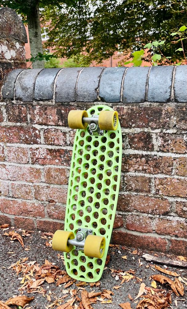 A green skateboard full of holes against a brick wall. 