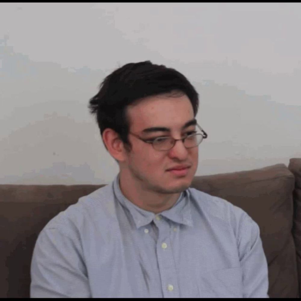 a man wearing glasses is sitting on a couch and making a funny face