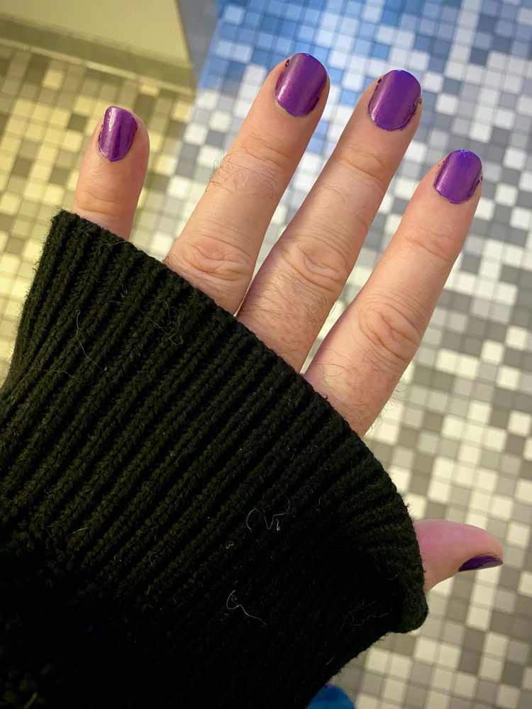 Picture of a hand with purple painted nails poking out of the sleeve of a black sweater. 