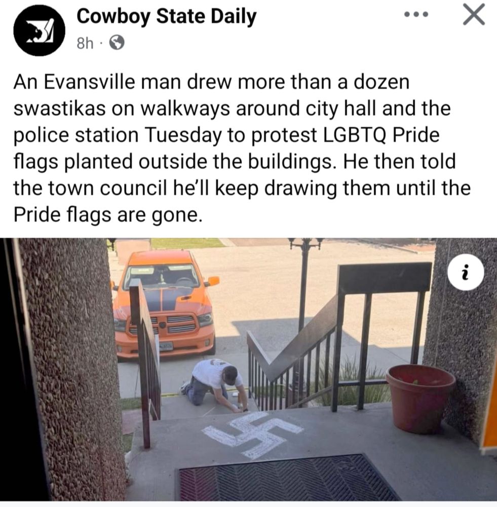 A Facebook post from Cowboy State Daily reports:

> "An Evansville man drew more than a dozen swastikas on walkways around city hall and the police station Tuesday to protest LGBTQ Pride flags planted outside the buildings. He then told the town council he’ll keep drawing them until the Pride flags are gone."

Below the text is a photo showing a man crouched on a sidewalk, actively drawing a large white swastika with chalk near the entrance of a public building. A bright orange vehicle is parked on the street in the background. The swastika is freshly drawn and highly visible in the center of the concrete walkway. The context and imagery convey a disturbing act of hate and intimidation tied to anti-LGBTQ+ sentiment.