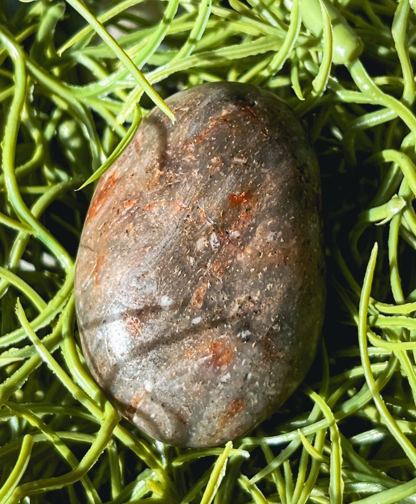 Small egg-shaped rock, beach polished. The rock is grey semi-translucent with streaks of red, gold, and white 