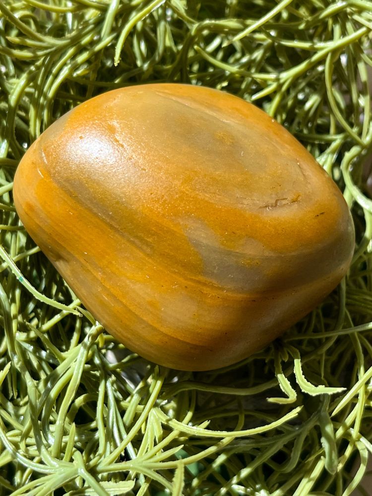 A beach-tumbled orange agate with dark bands sitting on greenery 