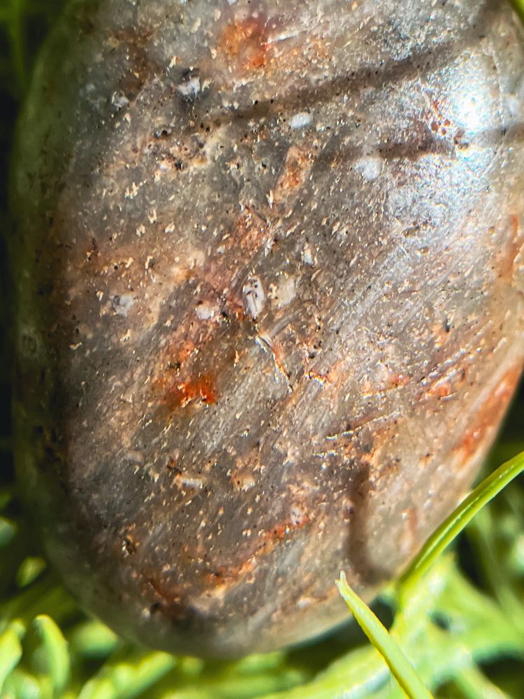 Small egg-shaped rock, beach polished. The rock is grey semi-translucent with streaks of red, gold, and white 