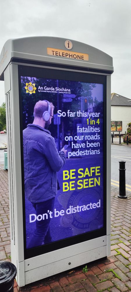A man with head phones and a phone walks

The sign says be safe be seen

Don't be distracted 