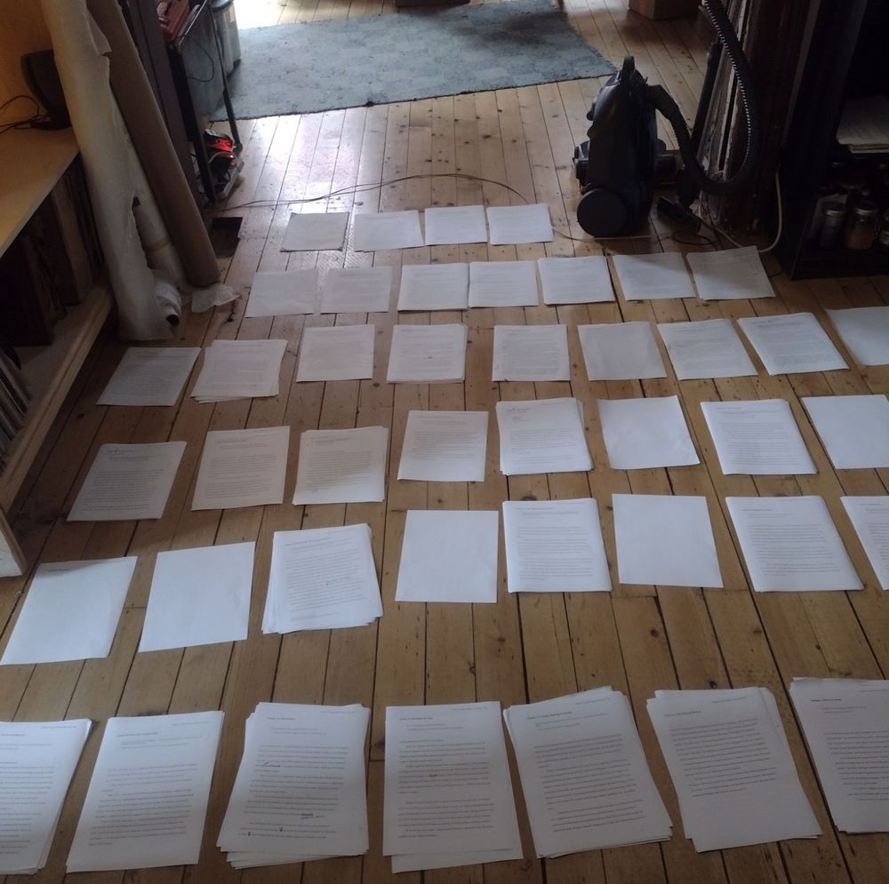 Two dozen or so small stacks of paper are arrayed on a hardwood floor.