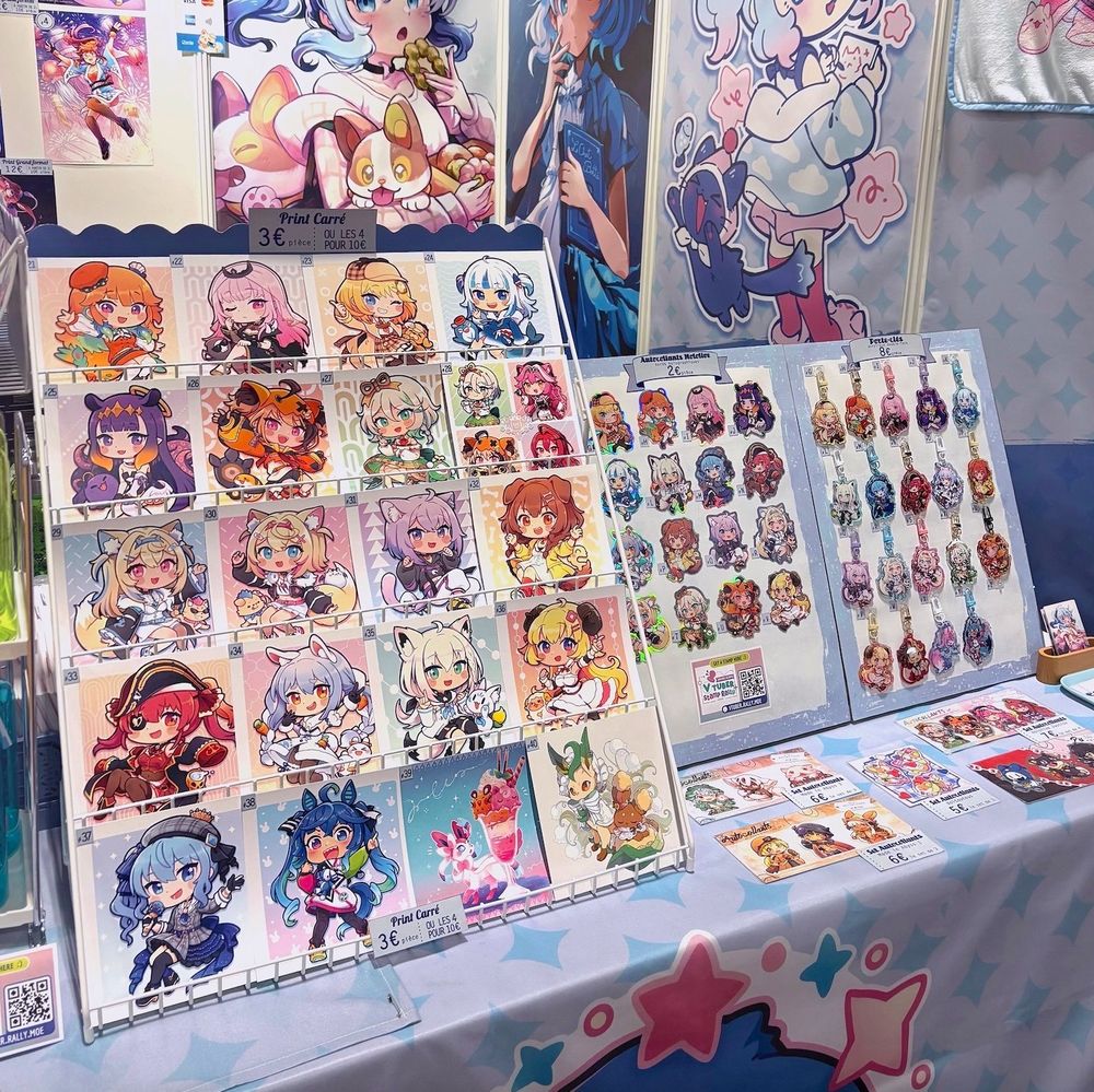 Close-up of another part of my booth at Japan Expo. It shows a rack full of prints, one display of stickers, and one of keychains. The art in there is mostly fanart (hololive) chibis.