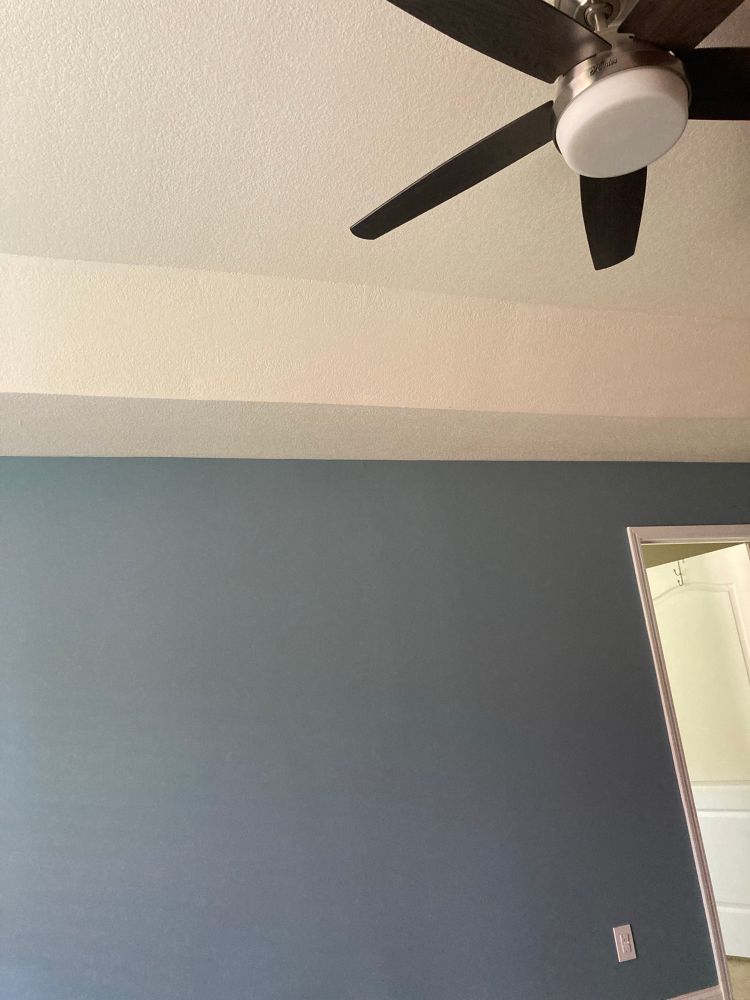 A photo showing a denim blue wall with white trim and ceiling. The blades of a black ceiling fan can be seen as well.