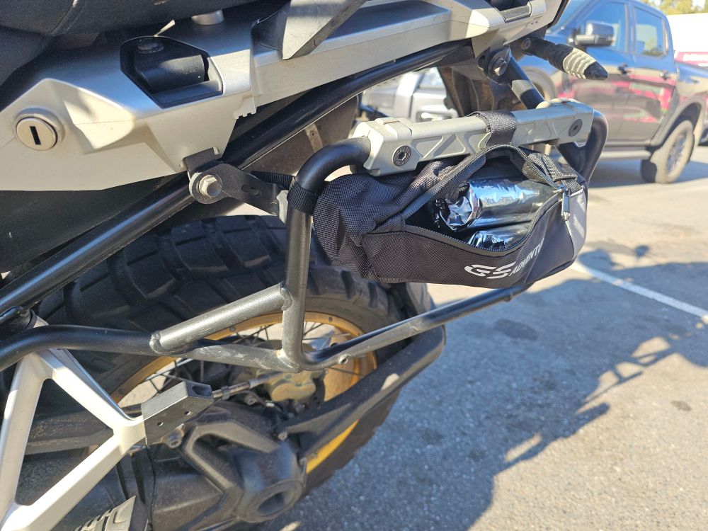 A small holster bag on the pannier rack of a motorcycle, with tube of crackers slid inside it. 