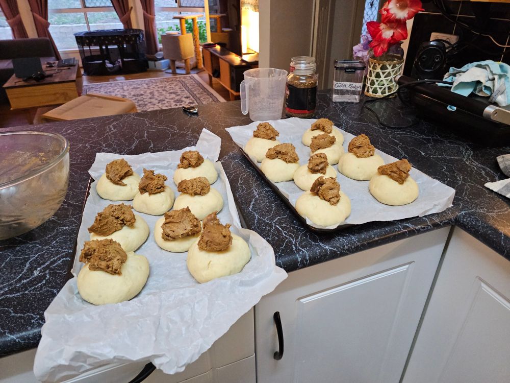 A bunch of coffee buns on pans ready to go in the oven