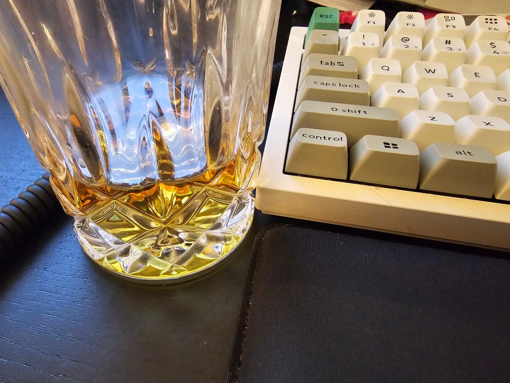 A glass of totally not alcohol beside a keyboard on a desk. 