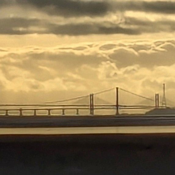 A close up of the right side of the silhouettes of the two Severn Bridge one behind the other, with an angry looking cloudy sky behind as the sun sets. 