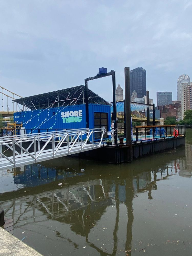 Shore Thing blue building on floating platform in a brown river