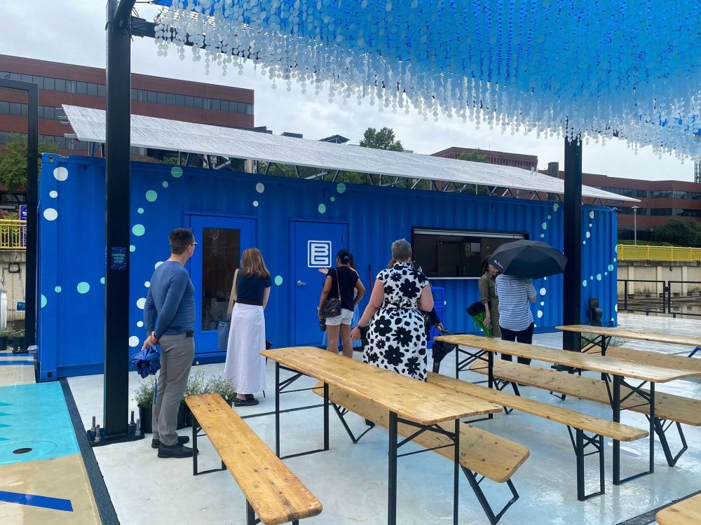 people stand in front of blue building and picnic tables