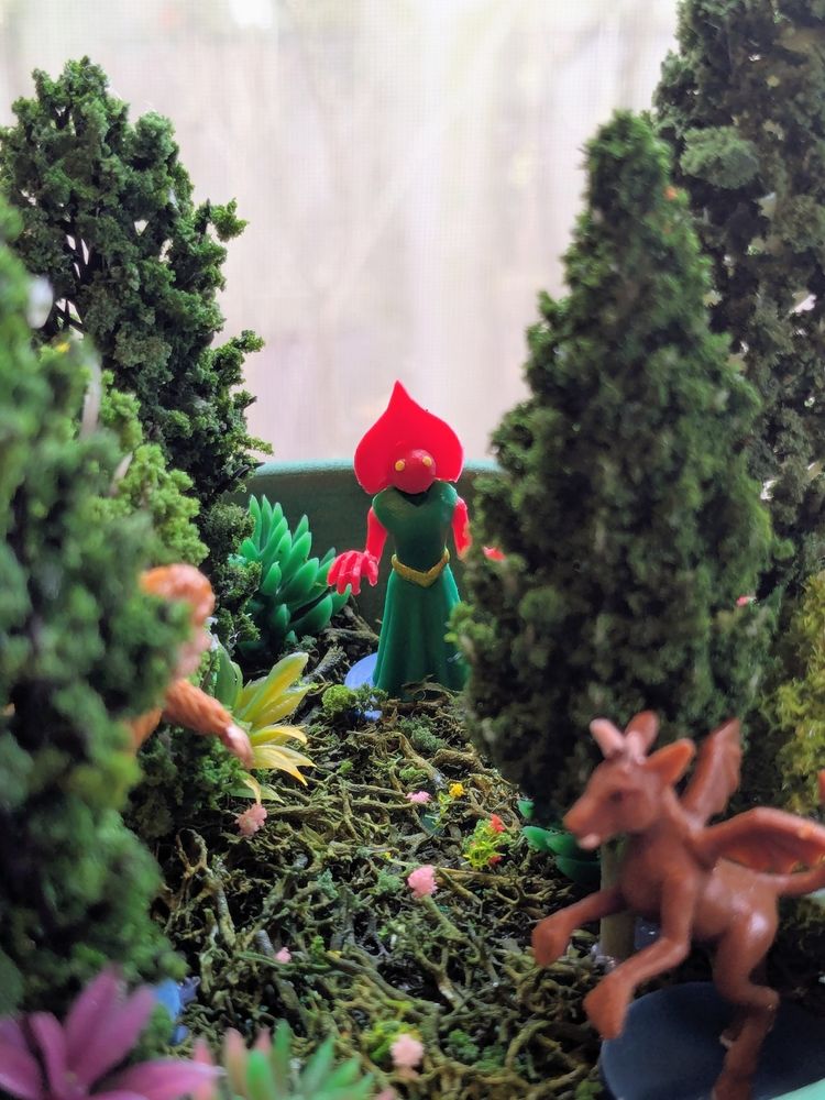 Close-up photo of a plastic Flatwoods Monster figure surrounded by miniature trees and plants.