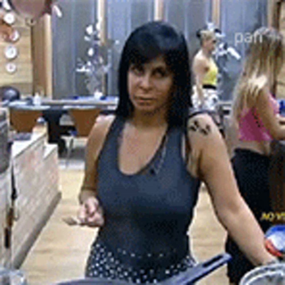 a woman in a tank top is standing in a kitchen holding a pan .