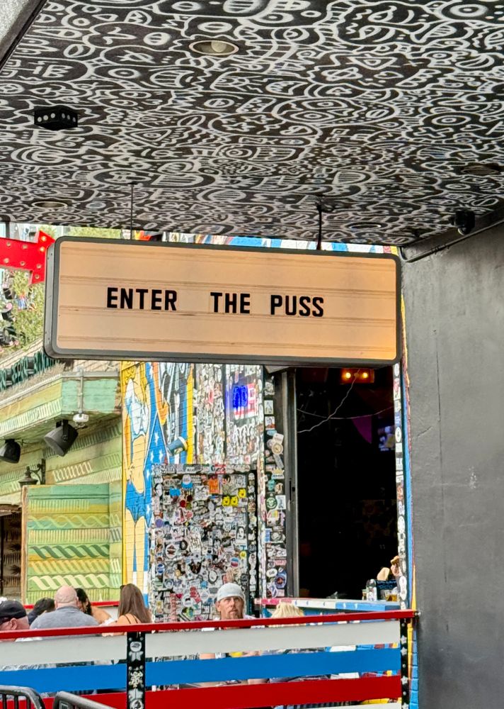 Marquee sign outside a bar saying, "enter the puss"