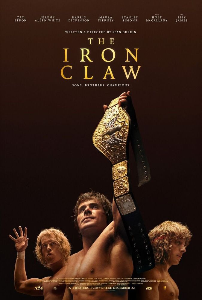 The Iron Claw movie poster - Zac Efron as Kevin Von Erich holding a gold championship belt with one arm above his head with David behind him on the left and Kerry behind him on the right.