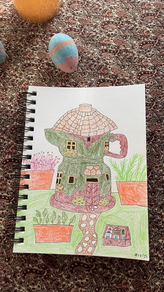 A sketchbook on a brown ornate table cloth. Toward the top left is a fake pink-blue egg. The colored pencil drawing has a green and brown moka pot house with red flower shrubs in the center. There are herb pots surrounding it. Also, a cobblestone pathway center and a mini garden accessory section on the right.