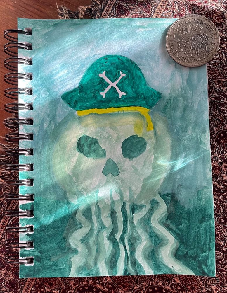 A sketchbook with a large silver coin holding down the right corner. The coin has a coat of arms on it. The watercolor art is a pale green jellyfish with a skull motif in the center. It is wearing a dark green pirate hat with a yellow-green sash.