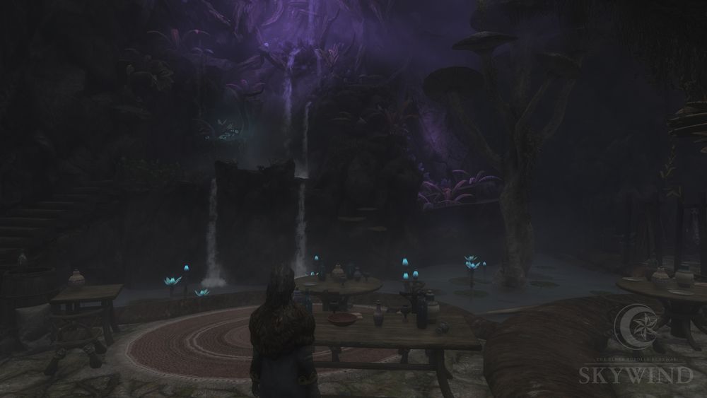 Picture of the interior of the tavern Fara's Hole in the Wall inside a mushroom, showing a larger seating area for guests, filled with tables. The room is a grand open space with a scenic view of a tall waterfall running alongside the opposite interior wall, leading down to a pool with lily pads situated below the seating area.