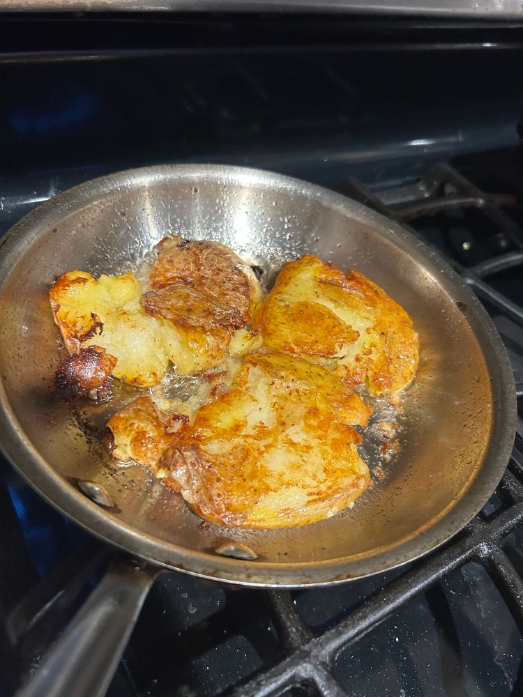 Salt potatoes frying in olive oil in a stainless steel pan.