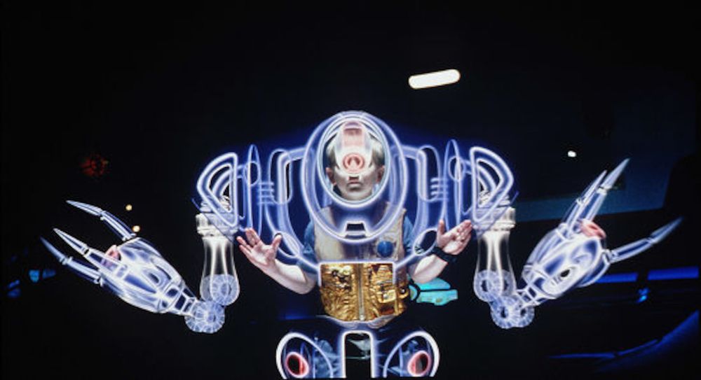 A screenshot from the 1998 Lost In Space movie. a young boy of about 10 years old stands at the ready with a holographic overlay of a robot surrounding him, as if he were inside the robot itself to pilot it.