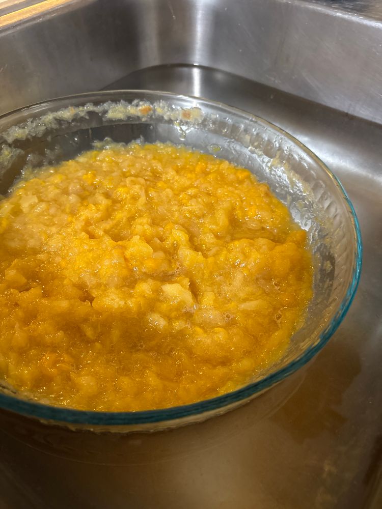 A clear glass bowl full of a lumpy yellow substance floats in a stainless sink full of water.
