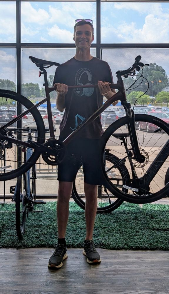 Tall man holding a new bike in front of store window. 